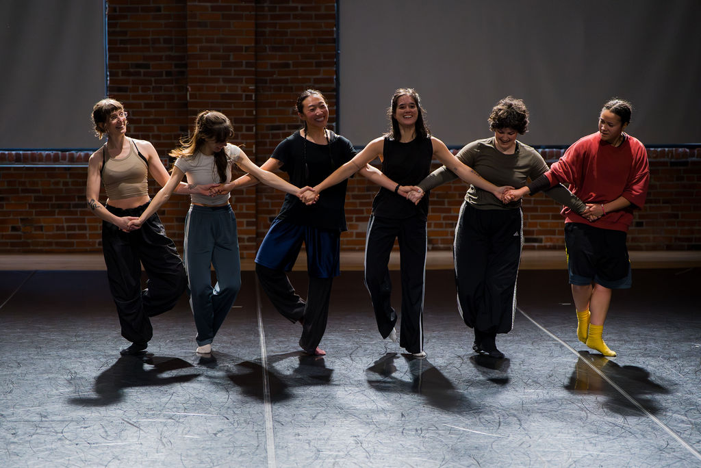 six whiplash dancers holding hands in a line across the stage